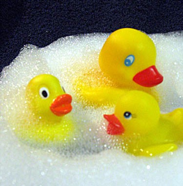 Three rubber ducks float in soapy water