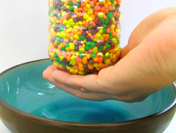 Hand at the bottom blocking the opening of a plastic bottle filled with candies