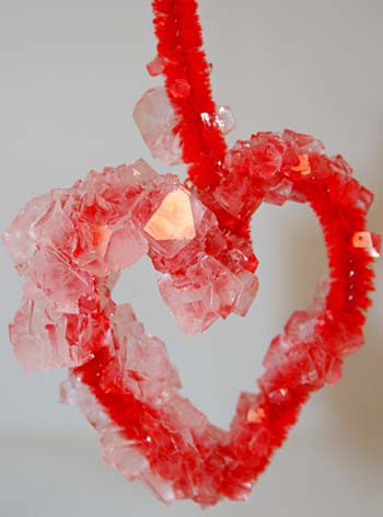 Translucent crystals form on a red pipe cleaner that is bent into the shape of a heart