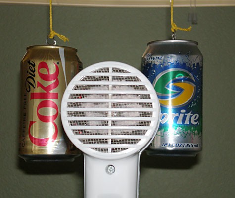 A hair dryer is aimed directly between two suspended soda cans