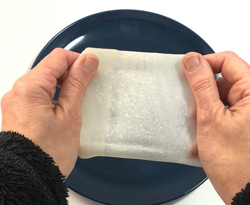 Two hands pulling on opposite edges of a square piece of edible paper.