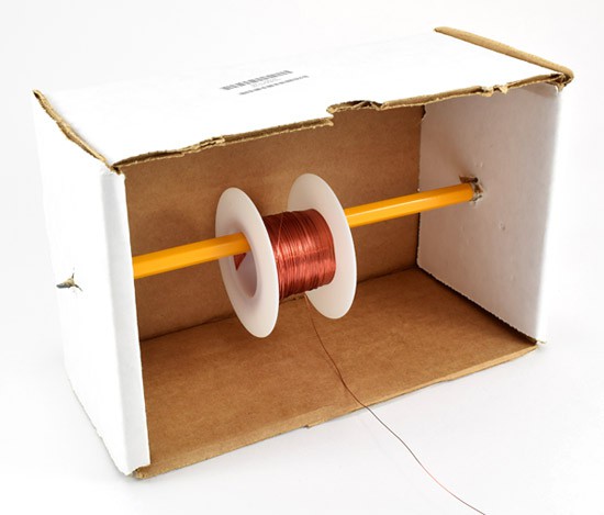 A wire spool hangs from a pencil that is pierced through the walls of a cardboard box