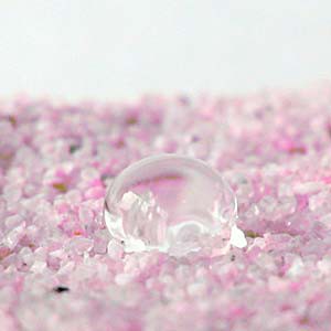 A bead of water rests on the surface of pink silica sand
