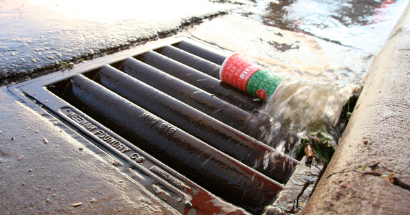 Storm drain on a street with water flowing and litter sitting on top of the drain