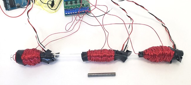 A clear plastic tube with three large wire coils wrapped around it 