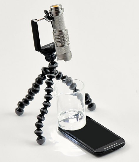 A flexible tripod holds a flashlight over a glass beaker that sits on the light sensor of a smartphone