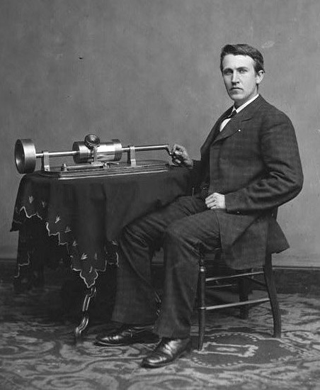 Black and white photo of Thomas Edison seated with a phonograph