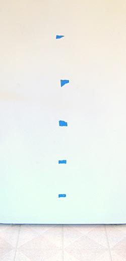 Strips of tape on a white wall placed vertically and spaced evenly apart