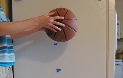 Hands about to drop a basketball against a background marked at intervals with tape.