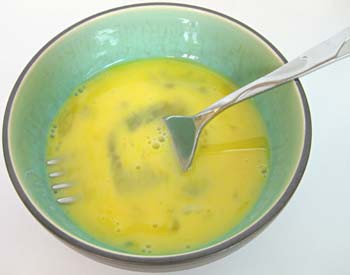 A fork is used to beat an egg in a bowl