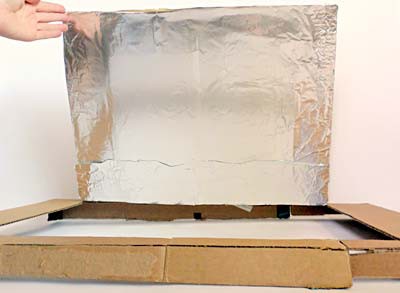 A large flap cut into the lid of a cardboard box is covered in aluminum foil