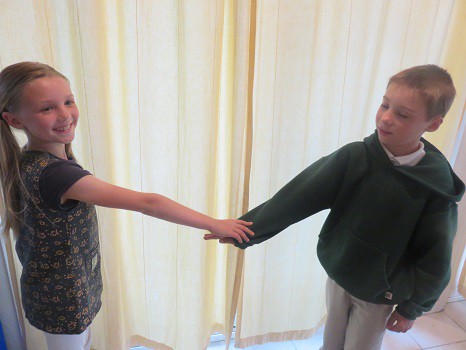 Two children facing each other with one arm sticking out, and one child pushing down on the other's arm