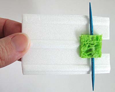 A toothpick and sponge rest on the end of a rectangular piece of styrofoam