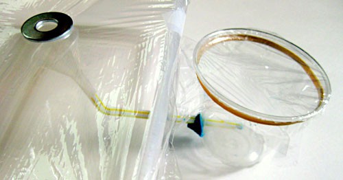 Saran wrap is placed over a collection cup used to catch condensation from a larger container