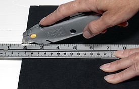 A utility knife cutting paper along a ruler