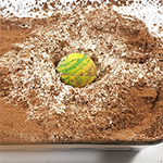 Dish of colored flour with a ball that has been dropped to demonstrate crater formation