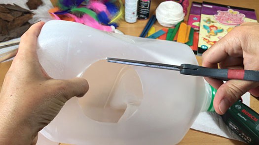 Scissors cutting a hole in the side of a plastic jug