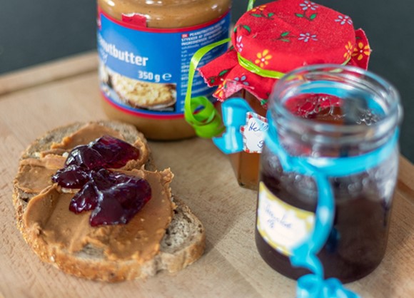 A peanut butter sandwich made by a robot with jars of jelly and peanut butter