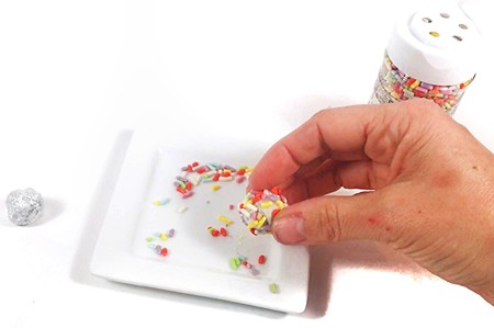 Hand holding an aluminum ball and rolling it in sprinkles.