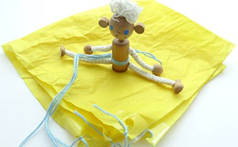 A wooden doll with a string harness and a tissue paper parachute