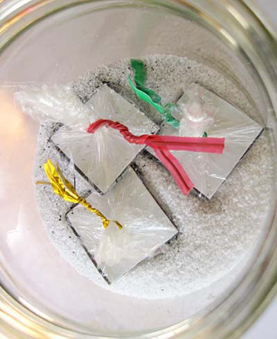 Three magnetic squares wrapped in plastic are dropped into a jar filled with iron filings and salt