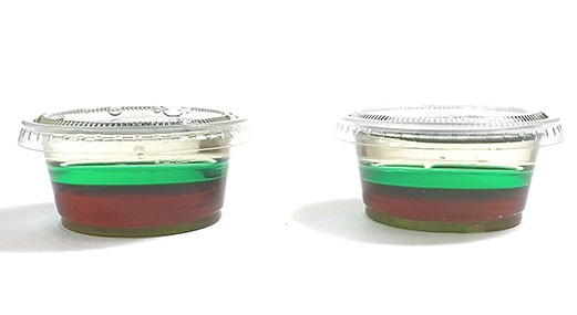 Two mini cups filled with corn syrup, green water, and vegetable oil and showing the layering of the different liquids. 