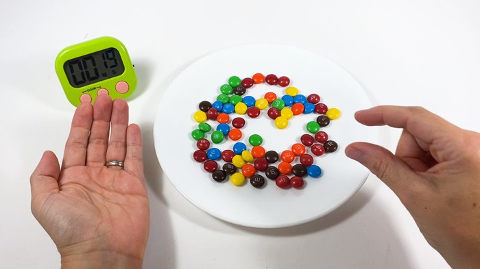 A hand picks up M&M candies off of a plate