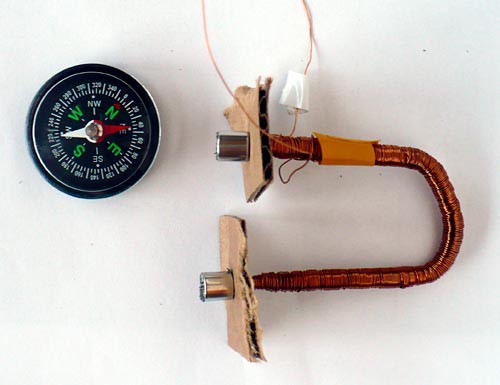 A U-shaped iron core, wrapped in wire, with cardboard and magnets on both ends of the core next to a compass