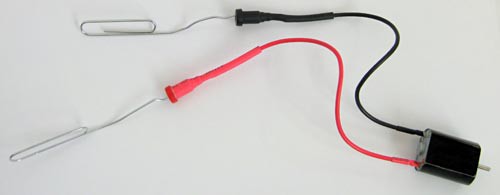 Bent paperclips are inserted into the two leads of a small motor