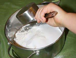 White powder is poured from a measuring cup into a metal mixing bowl