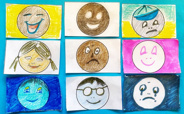 A blue paper with 6 happy and sad face drawings. The drawings are colorful.   