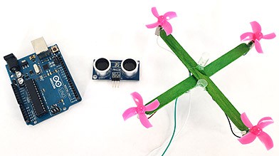 A popsicle stick drone next to an ultrasonic distance sensor and an Arduino 