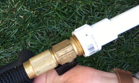 A PVC adapter piece connecting a garden hose to a PVC pipe.  