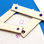 Pantograph device made from cardboard and office supplies and shown being used to duplicate an image