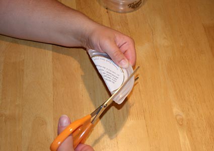 A hole is cut in a circular plastic lid with scissors