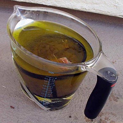 A reusable coffee filter is filled with coconut husks and submerged in a measuring cup filled with oil and water