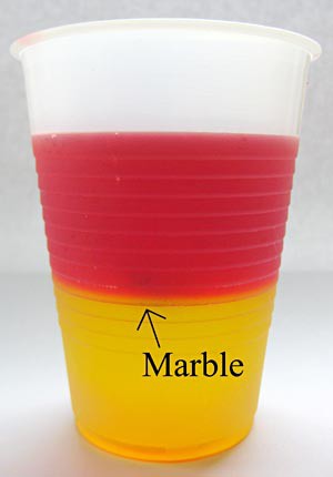 A cup contains two layers of different colored JELL-O that has a marble trapped between the two layers