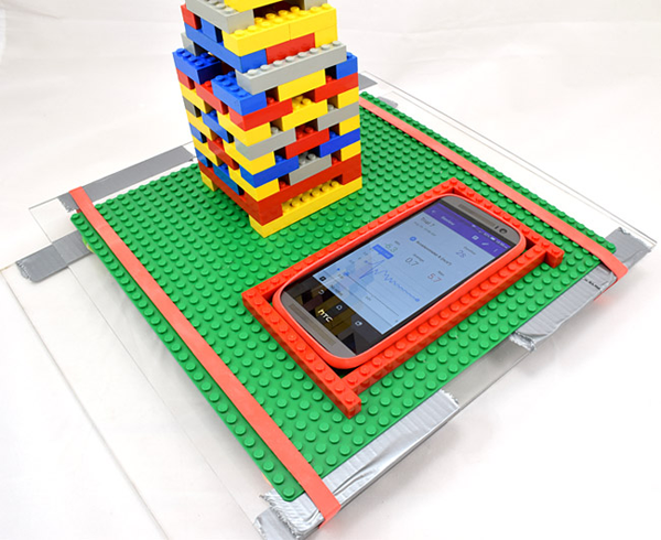 A smartphone using the Google Science Journal app lying on a shake table next to a LEGO building