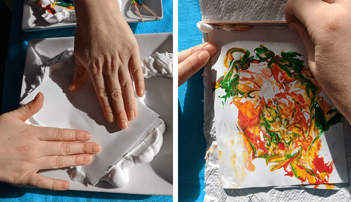 Student carefully pressing card on top of the food coloring and shaving cream-covered plate and then scraping excess shaving cream off the marbled art card
