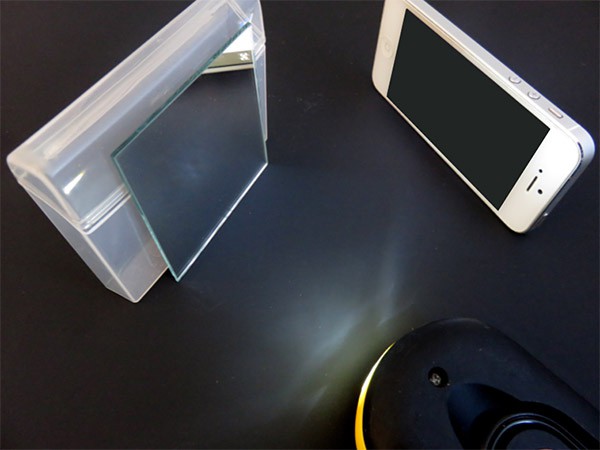 A flashlight reflects off a mirror towards a phone which measures the intensity of the light