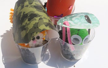 Toy animals sit in cups with coverings over their heads