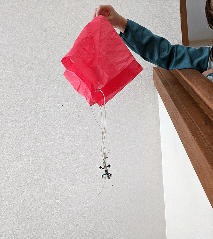 Student holding homemade parachute from the top of a stairwell landing and preparing to drop it to the bottom