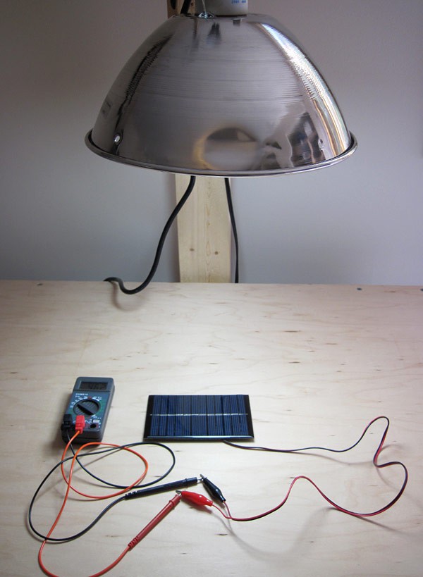 A lamp shines on a solar panel that is connected to a multimeter