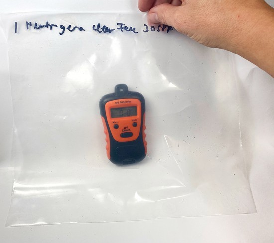 A hand holds a plastic sheet in front of a UV meter device. 