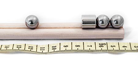 A magnet with two metal balls attached to one end rests on a rail next to a third metal ball