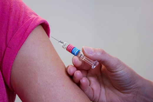 Vaccine shot being administered to someoneâ€™s bare arm. 