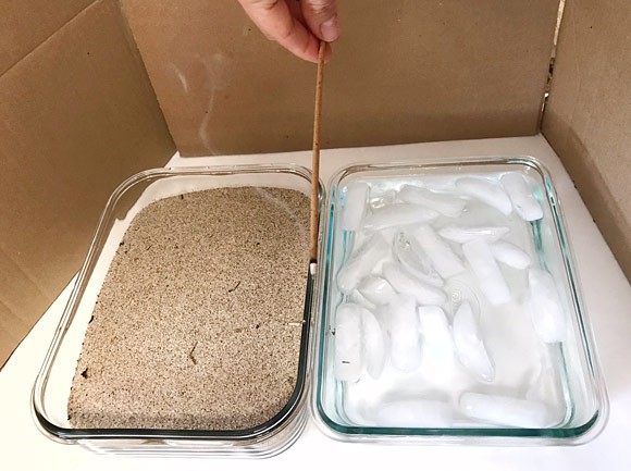 An incense stick is held between two containers filled with sand and ice water