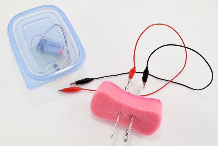 Alligator clips connect two leads from a moisture sensor to sticks of foil that are inserted through the center of a sponge