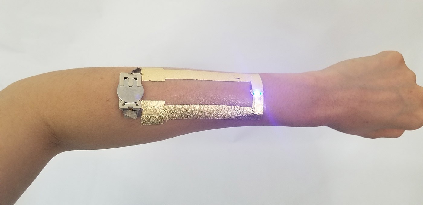 A circuit made from metal foil with a coin cell battery and an LED on a person's forearm 