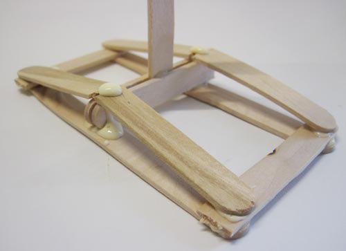Four popsicle stick halves secure a support stick base to a rectangular base made from popsicle sticks